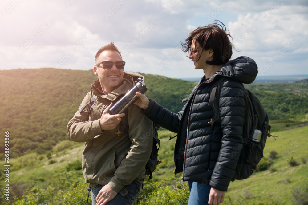 Male hiker giving thermos to his girlfriend Male hiker giving thermos to his girlfriend