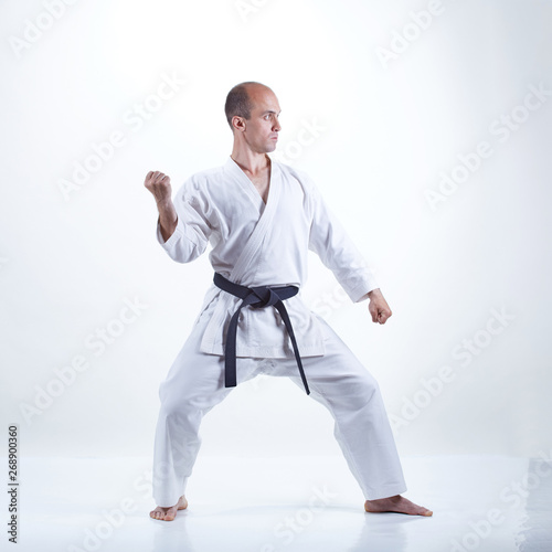 On a light background, a young athlete with a black belt is doing formal karate exercises