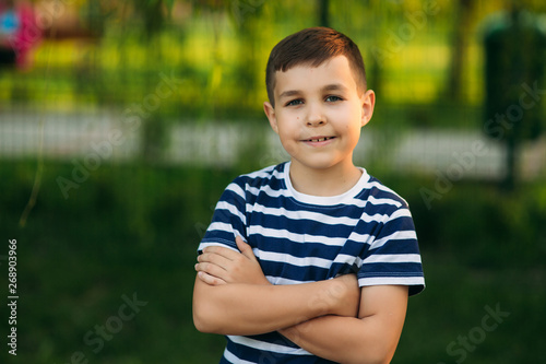 A little boy in a striped T-shirt standing in front of green background. Smiling and looking to the photographer