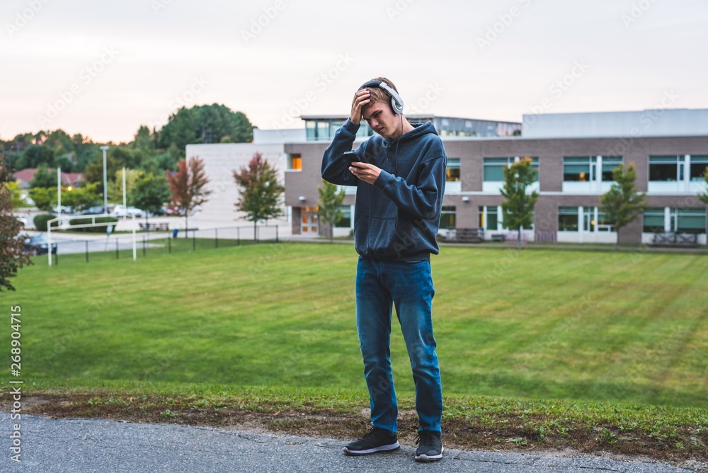 Upset teenager listening to music with his headphones on an overcast day.