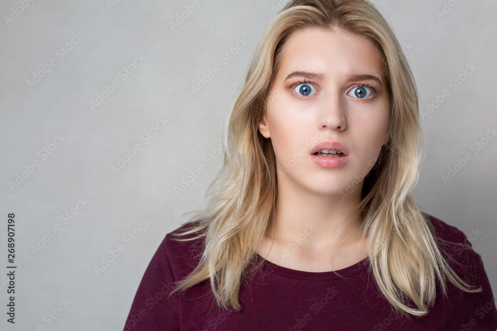 Closeup shot of shocked young woman standing over a grey wall. Empty space Closeup shot of shocked young woman standing over a grey wall. Empty space