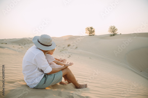 Father sitting with his daughter on the sand in the desert