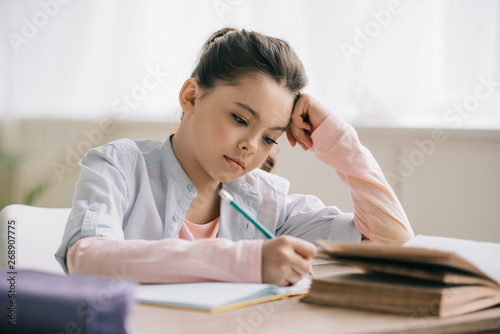 thoughtful schoolchild writing in notebook while sitting at desk and doing homework © LIGHTFIELD STUDIOS