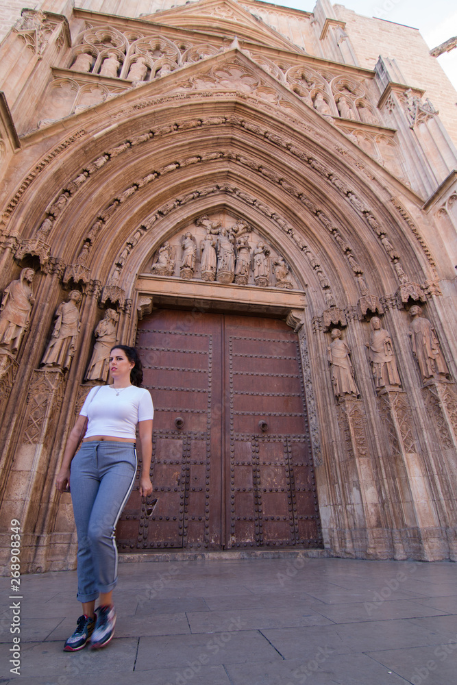A young brunette woman walking in front of the Cathedral of Valencia (Spain) with white shirt and gray pants
