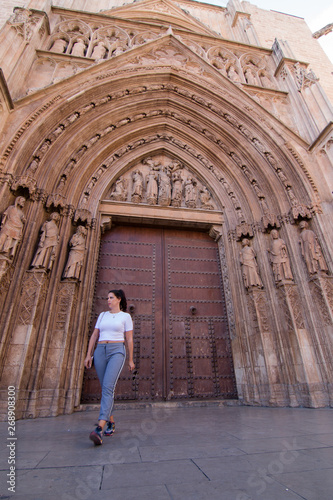 A young brunette woman walking in front of the Cathedral of Valencia (Spain) with white shirt and gray pants