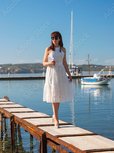 young woman walking with book in hand by pier in yacht club 