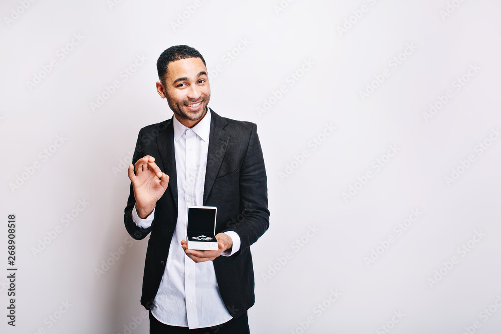 Happy handsome guy in luxury white shirt, black jacket holding gift and smiling to camera on white background. Holidays time, making surprise, ornamentation, cheerful mood Happy handsome guy in luxury white shirt, black jacket holding gift and smiling to camera on white background. Holidays time, making surprise, ornamentation, cheerful mood