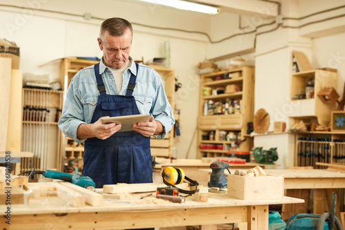 Waist up portrait of senior carpenter using tablet while working in joinery, copy space