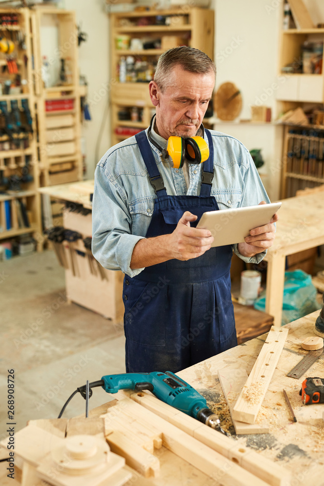 Portrait of modern senior carpenter using digital tablet while working in joinery Portrait of modern senior carpenter using digital tablet while working in joinery
