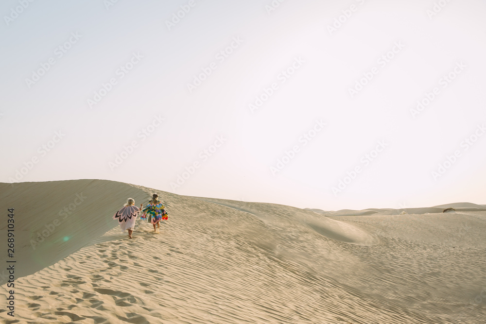 Two girls wearing colorful hand made wings and running in the desert Two girls wearing colorful hand made wings and running in the desert