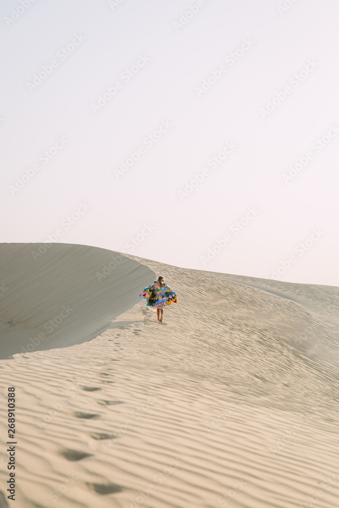 Little girl with colorful wings running in the desert during the sunset