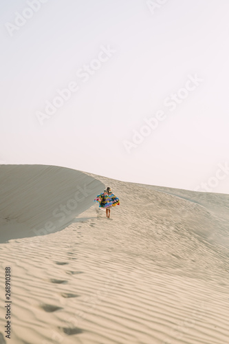Little girl with colorful wings running in the desert during the sunset