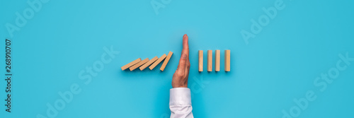 Male hand stopping falling dominos photo