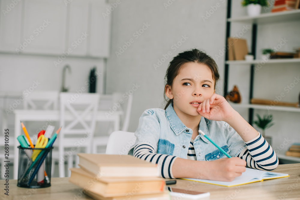 thoughtful child looking away while sitting at table and doing homework thoughtful child looking away while sitting at table and doing homework