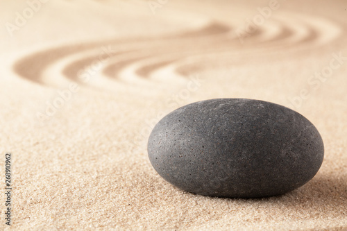 Spiritual stone therapy, black basalt round rock on sandy background. Spa wellness treatment.