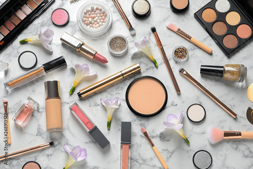 Many different makeup products and spring flowers on marble background, flat lay