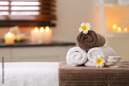 Fototapeta Naklejka Na Ścianę i Meble -  Composition with towels, flowers and stones on massage table in spa salon. Space for text