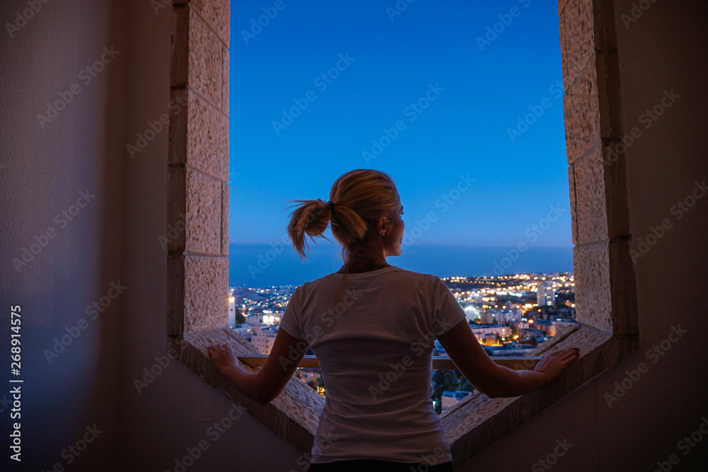 woman is looking at night city. woman silhouette in the window of a skyscraper. Dark outline woman watching traffic night city.