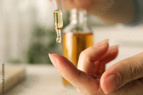 Woman dripping essential oil on finger at table, closeup