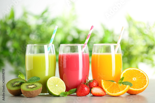 Glasses of different juices with straws and fresh fruits on table against blurred background