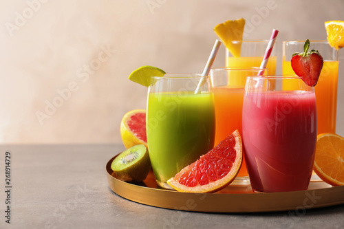 Tray with glasses of different juices and fresh fruits on table. Space for text