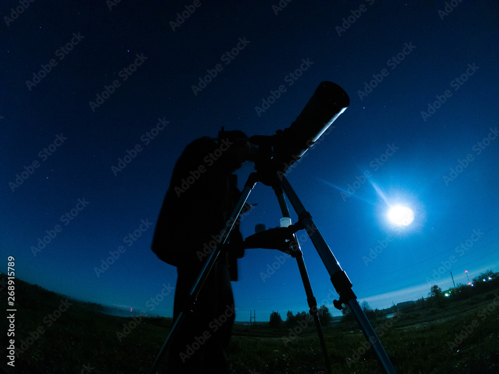 A man looks at the stars at night through a telescope.
