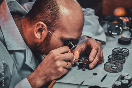 Undistracted clockmaster is fixing old watch for a customer at his own workshop. photo