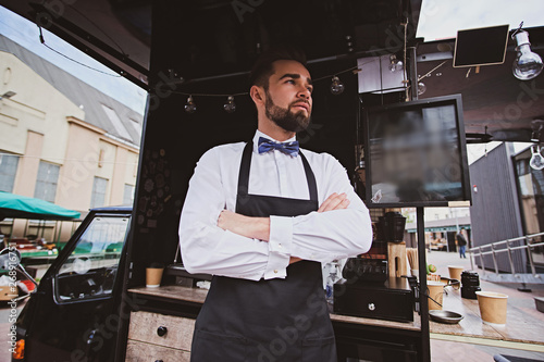 Handsome elegant barista is standing crossed his hands next to his coffeeshop.