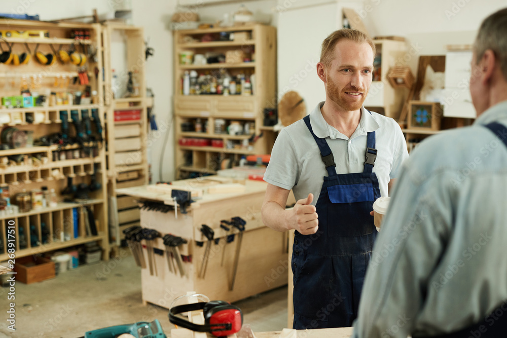 Portrait of young carpenter talking to senior worker during coffee break in workshop, copy space