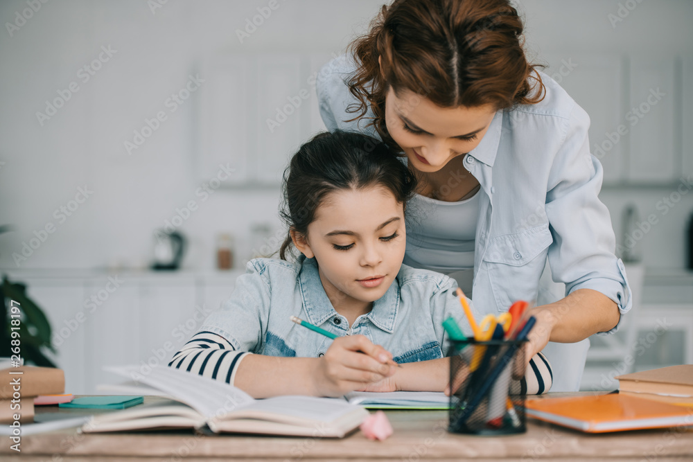 adorable child writing in copy book while doing schoolwork near mother adorable child writing in copy book while doing schoolwork near mother