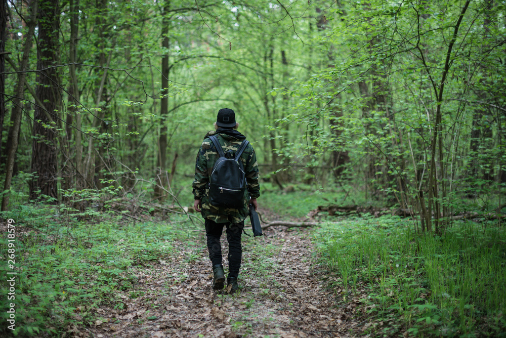 A young man in a camouflage jacket is walking along a forest path, view from the back
