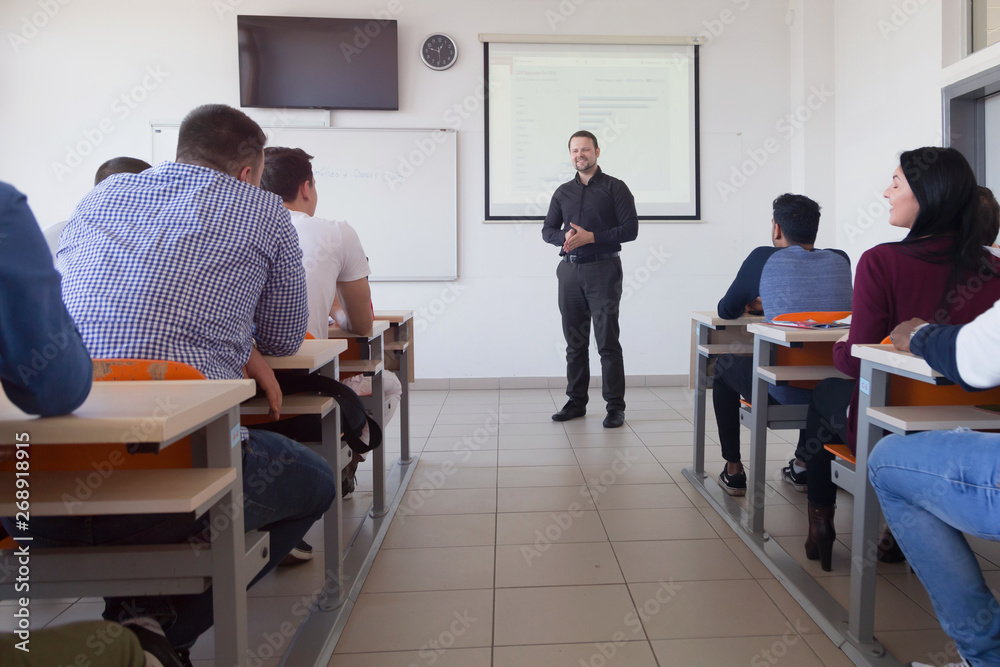 Male professor explain lesson to students and interact with them in the classroom.Helping a students during class. University student being helped by male lecturer during class.