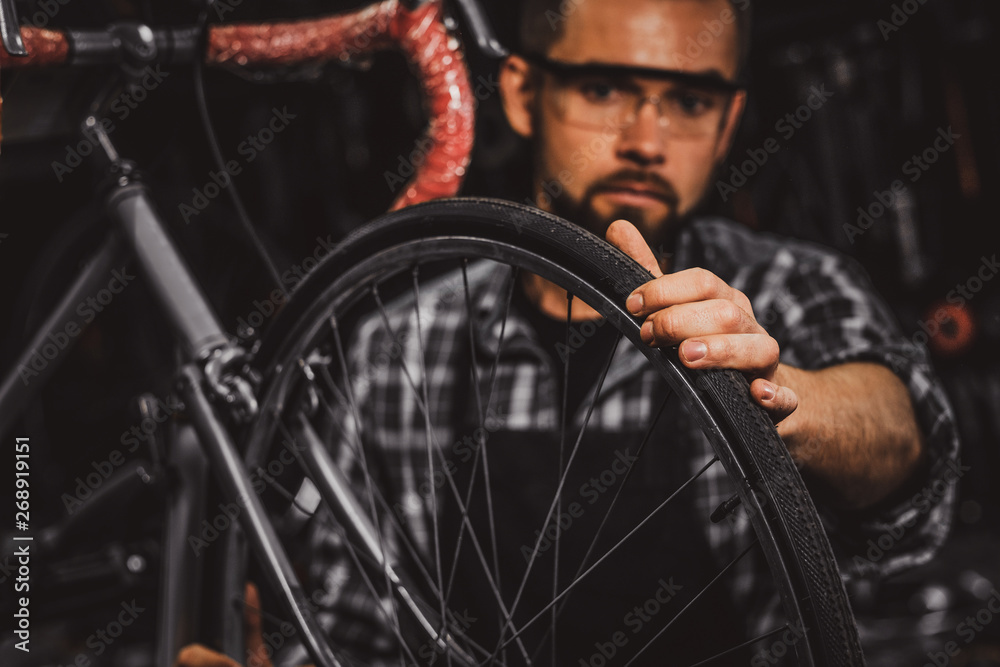 Handsome serious man in protective glasses is fixing bicycle at his own shop. Handsome serious man in protective glasses is fixing bicycle at his own shop.