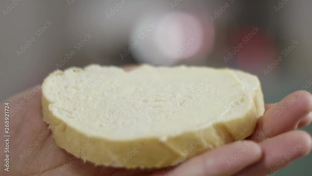 Closeup slow motion view of male hands holding slice of white wheat bread and spreading fresh yellow butter on its surface with silver knife in daylight kitchen. Closeup slow motion view of male hands holding slice of white wheat bread and spreading fresh yellow butter on its surface with silver knife in daylight kitchen.