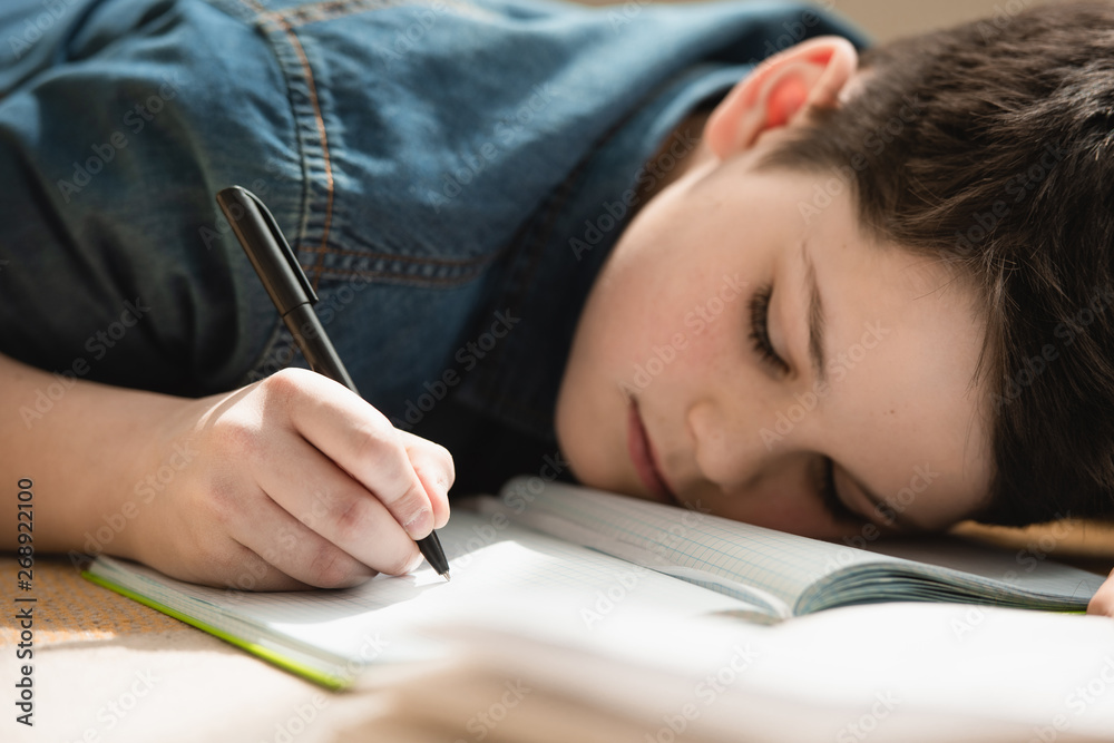 exhausted boy lying on floor and writing in copy book while making schoolwork at home exhausted boy lying on floor and writing in copy book while making schoolwork at home