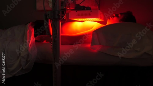 Camera remains static on patient that is lying on back under the infrared lamp at chest level photo