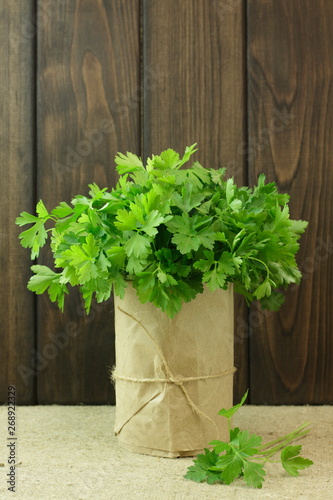 Green parsley in a paper glass on a background of wooden texture.