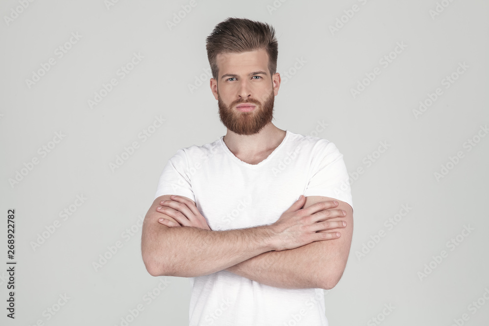 Portrait of a beautiful sexy hipster dressed in a white T-shirt. hold hands crossed and looking to the camera. he stands upset in front of the white background