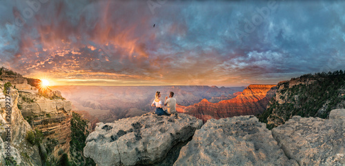 Man and woman sit on the edge of rim talking about future and watching the Grand Canyon sunset while bird in the sky