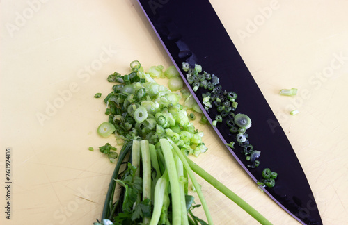 Bunch of greens with a black knife on the table. Chopped greens on the table. Crushed greens on a yellow Board with a black knife. Black knife, and a bunch of greens
