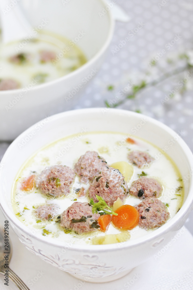 creamy soup with meatballs in a white bowl on the background of a gray tablecloth in polka dots. light soup with cream and pork meatballs. French style dishes. SWEDISH MEATBALLS