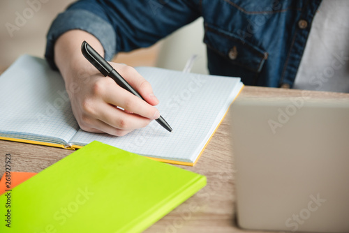 cropped view of schoolboy writing in notebook while doing schoolwork at home photo