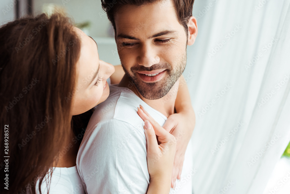 attractive girl hugging happy man standing in white t-shirt at home attractive girl hugging happy man standing in white t-shirt at home