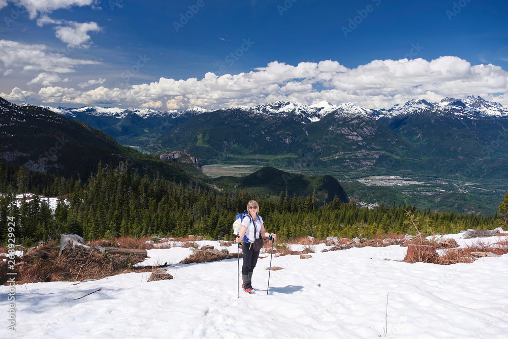 Active vacation near Whistler, BC. Smiling middle age woman hiking on mountain top with scenic view of Squamish, Tantalus Ridge and Stawamus Chief peaks. Garibaldi Provincial Park. BC. Canada.