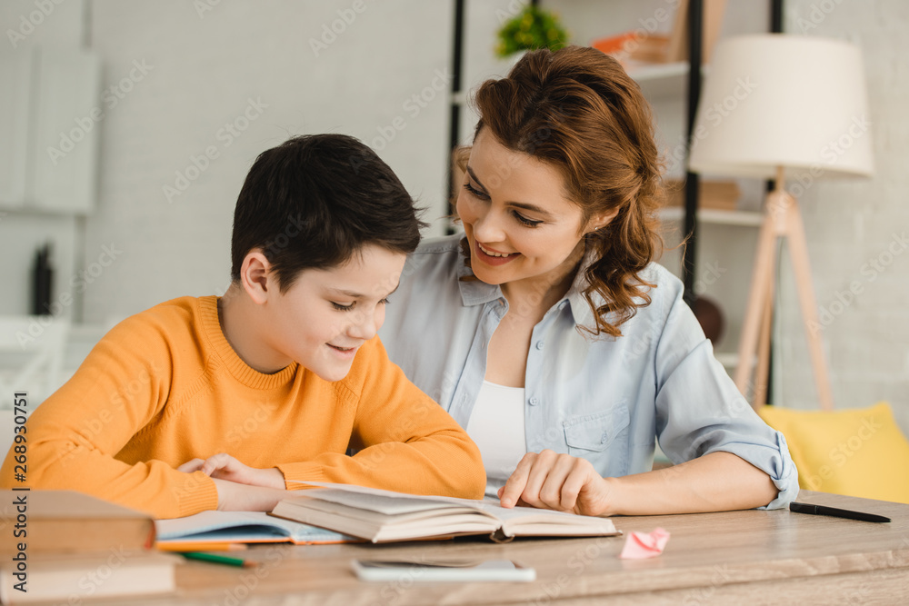 smiling mother helping adorable son doing schoolwork at home smiling mother helping adorable son doing schoolwork at home