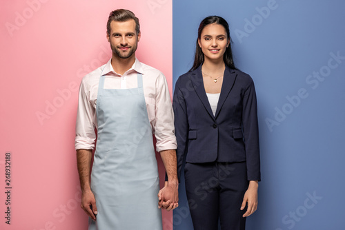 smiling man in apron and businesswoman holding hands on blue and pink photo