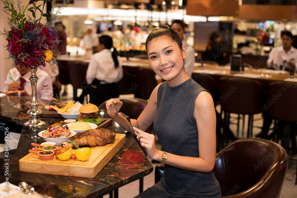 Working Asian Woman Black hair having Lunch big piece Steak grill Dinner of Western food in fusion restaurant cafe and eat alone. Concept enjoy eating myself for good food life