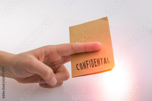 Hand holding a brown color paper with text confidental photo