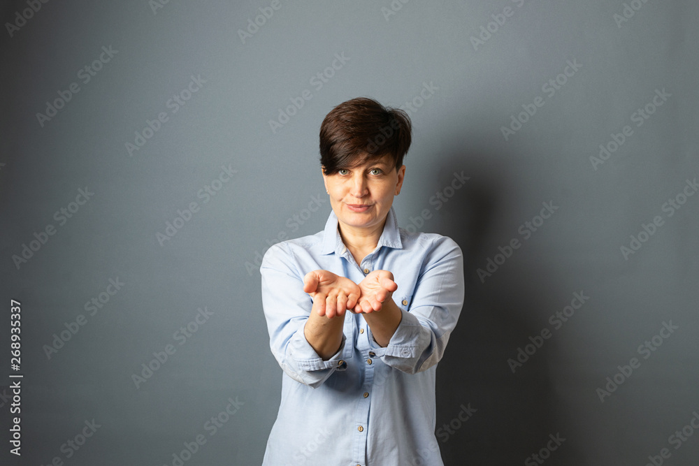 Woman stretches empty hands palms forward. Woman portrait on a gray background. Copy space. Woman stretches empty hands palms forward. Woman portrait on a gray background. Copy space.