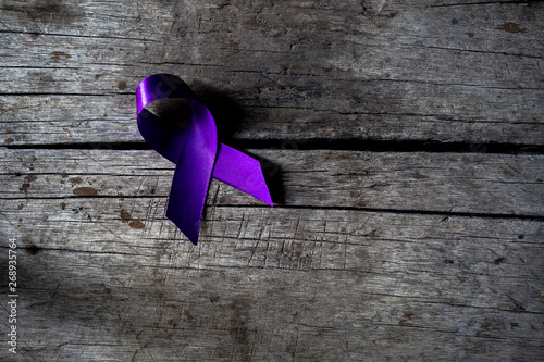 a purple ribbon for the awareness about the unacceptability of the violence against women, on a dark gray rustic wooden surface photo